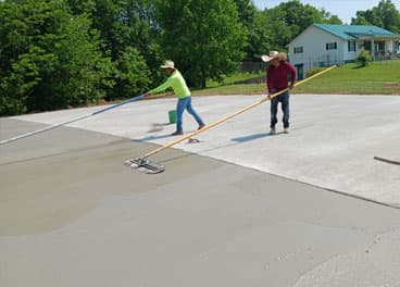 Two-man crew finishing a large concrete pad with bull floats on a sunny day in Lawrence County