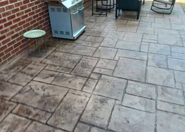 Stamped concrete patio with natural stone pattern next to a brick home with outdoor grill area